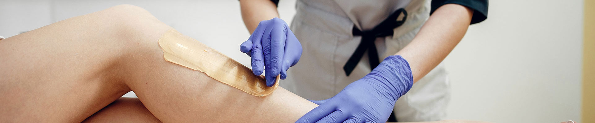 Aesthetician applying wax on a client's leg for hair removal.