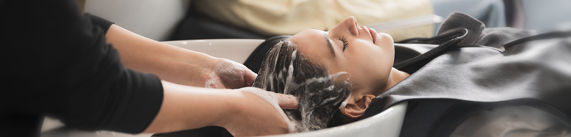 Hair being washed in a salon basin by a hairstylist wearing black.