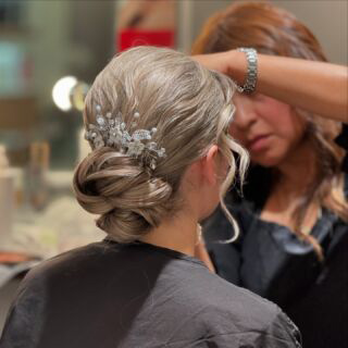 Stylist applying finishing touches to a client's elegant updo hairstyle adorned with delicate hair accessories.