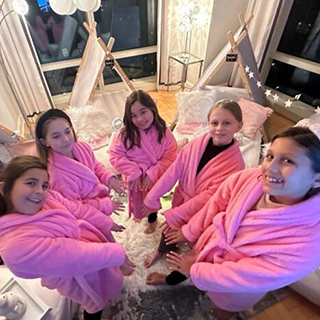 A group of girls in pink robes smiling and posing together for a cheerful photograph.