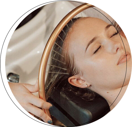 A woman relaxing while receiving a hair treatment under a circular water shower at a salon.