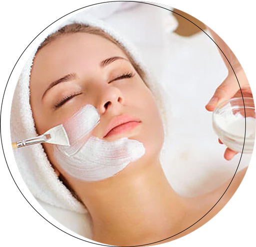 A woman receiving a facial treatment with a brush applying a white cream mask to her face in a spa setting.